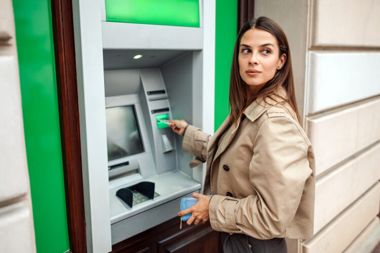 una mujer mira hacia atrás mientras introduce su tarjeta en un cajero automático de la vía pública